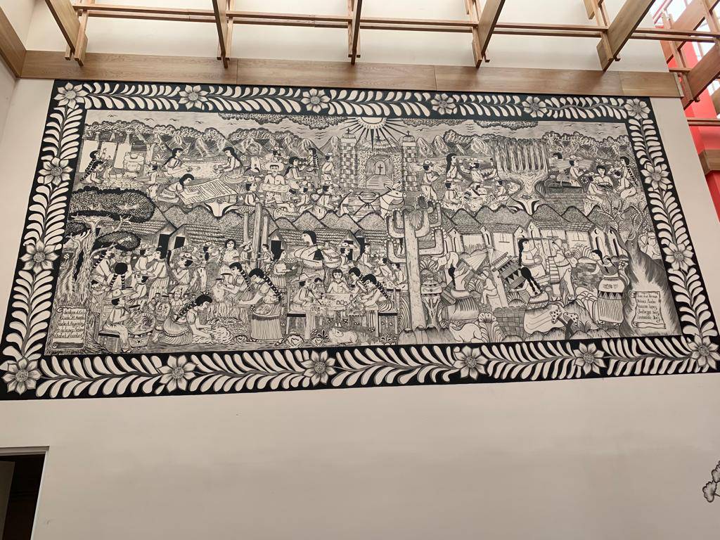 Foto completa del mural colectivo que ilustra la Galería del Fondo Nacional para el Fomento de las Artesanías (FONART), ubicado en el Centro Cultural Los Pinos. Esta obra es una pieza colectiva elaborada por distintas manos que mantuvieron un mismo estilo gráfico: trazos sencillos que ilustran la cotidianidad del mercado tradicional mexicano.